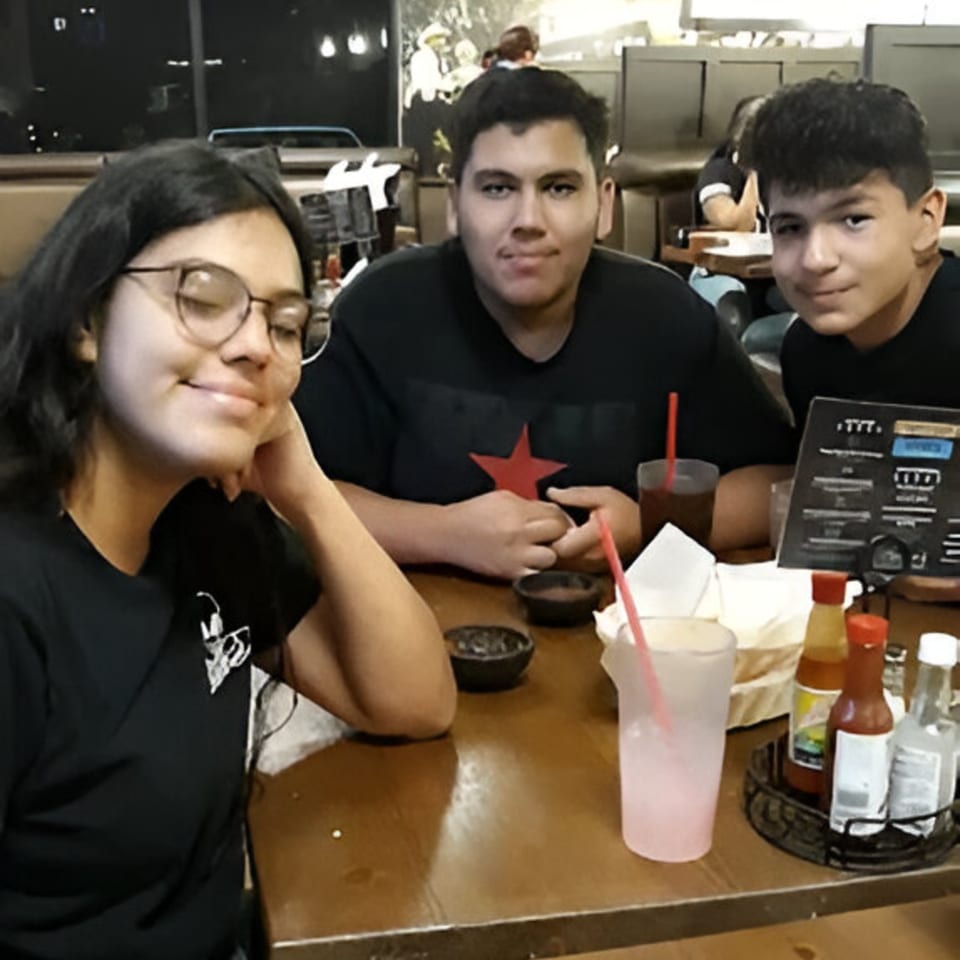 Three young people sitting at a table in Ruben's Mariscos and Mexican Grill, with drinks and condiments.