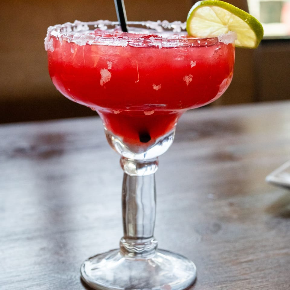 A vibrant red margarita with a salted rim and lime wedge, served in a classic glass.