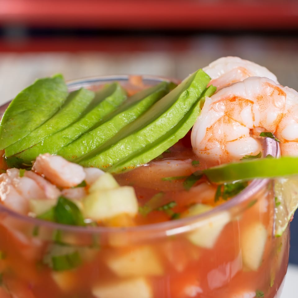 Close-up of a Mexican shrimp cocktail with avocado slices and a lime wedge.