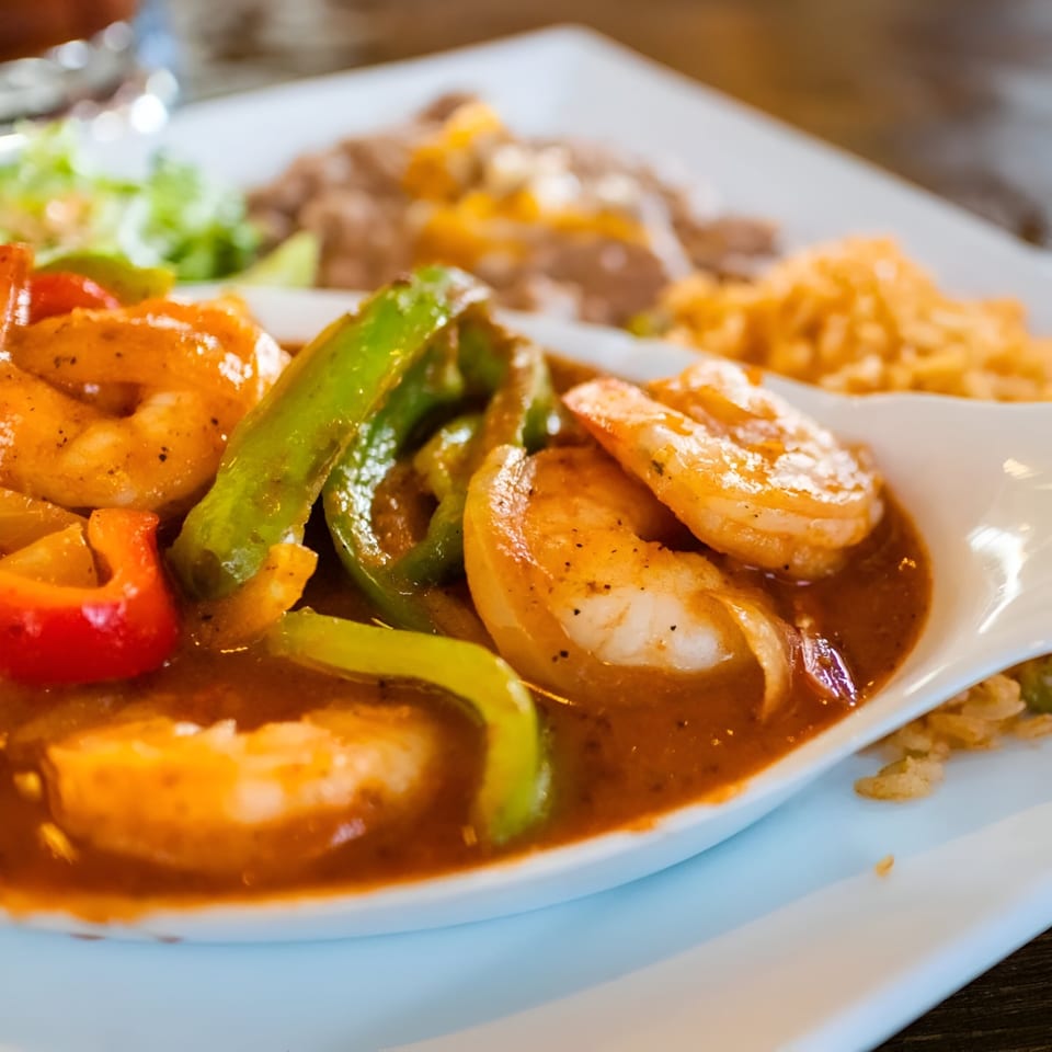 Shrimp fajitas with bell peppers in a rich sauce, served with rice and refried beans.